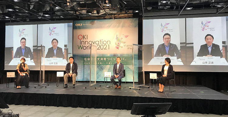OKI Innovation World 2021におけるYume ST TAKASAKIとのリアルタイム中継（後ろのディスプレイにYume ST TAKASAKIからの参加者を投影）の写真